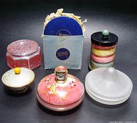 Front view of all powder jars, containers, and box of puffs showing different shapes, materials and colors.