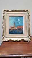 Full view of framed oil painting showing Venice cityscape with water, gondolas, and architecture, in gold-colored ornate frame.