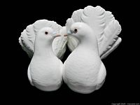 Front view of porcelain figurine showing two white doves facing each other with detailed feathers and large fanned tail feathers.