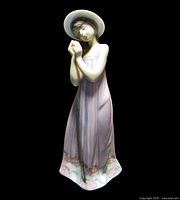 Front angled view of the Lladro figurine showing the girl holding a flower with both hands and wearing a long lavender dress with floral trim and a white wide-brimmed hat.