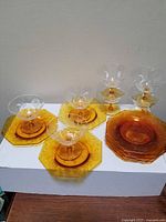 Set showing 8 amber sherbet glasses each paired with 8 octagonal amber underplates on a white surface against a plain wall.