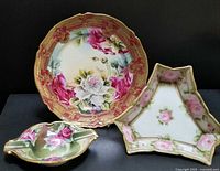 Lot of three Nippon porcelain pieces with rose decoration and gold detailing: plate, footed dish, cigar ashtray, shown together on black background.