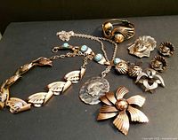 All items of the lot displayed on black background showing variety of copper jewelry including necklaces, bracelets, brooches, and earrings.