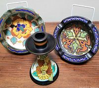Set of three Gouda pottery pieces displayed together, showing candlestick and two ashtrays with colorful floral and abstract designs.