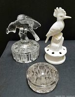 Full lot view showing three flower frogs: clear glass parrot figural, white porcelain bird, and small domed glass frog.
