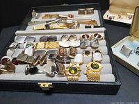 Full display of cufflinks and tie bars in an open case with boxed cufflink sets visible to the right