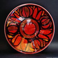 Top view of shallow round bowl with bright abstract decoration in reds, oranges, yellows, and black lines.