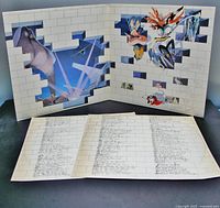 Gatefold album cover opened showing colorful 'The Wall' album artwork, including illustrations and brick wall motif, with printed lyric sheets or inner sleeves laid out.
