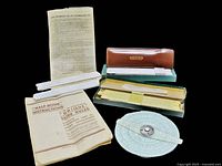 Slide rules arranged with instruction guides, showing condition and accessories including leather case and boxes.