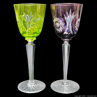 Pair of two vintage tall stemmed cut-to-clear crystal wine glasses in plum and chartreuse colors on black background.