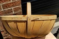 Close-up photo showing side profile of vintage split wood apple basket with bentwood handle attached and the vertical wood slats form sides.