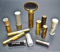 Lot of 11 vintage European lipsticks and eyeliners in various metal tubes and containers with decorative vintage labels and engravings and a lipstick with an attached mirror.