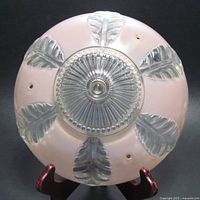 Top view of a round pink glass ceiling light shade with central clear glass decorative disc and six clear glass embossed leaves.