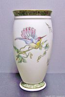 Front view of the vase showing a flying hummingbird on a branch with pink and green leaves, green floral border with gold trim at rim and base.