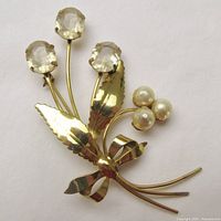 Front angled view of the gold vermeil floral brooch showing three faceted pale yellow citrine paste flowers, faux pearl cluster, two leaves, and bow detail.
