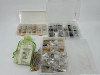 Overview photo showing three open plastic boxes with compartments filled with assorted jewelry findings in gold and silver tone, along with a green drawstring bag containing additional small bags.
