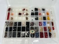 Top-down view of one clear plastic organizer box with multiple compartments holding a wide variety of small beads in black, brown, orange, yellow, red, blue, and clear tones.