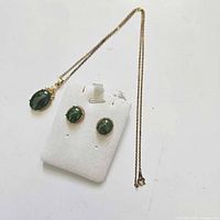 Necklace with green oval stone pendant and matching earrings with round green stones on white display pad
