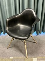 Side angled view showing the black molded plastic seat with armrests and natural wooden legs on carpet.