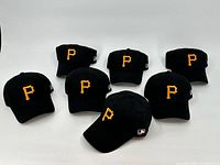 Seven black Pittsburgh Pirates baseball hats arranged in two rows showing yellow embroidered 'P' logo fronts