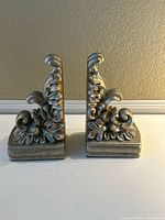 Pair of ornate ceramic bookends shown side by side on flat surface against wall.