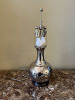 Full view of the silver metal lamp on marble surface, showing overall shape and finish