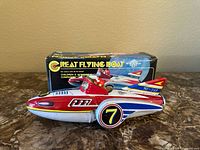 Front view of the vintage flying boat toy with the box behind it showing the toy and packaging details.