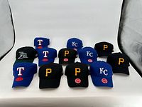 Photo showing all 12 baseball caps arranged facing forward, displaying logos of each cap