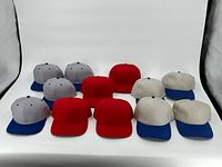 Photo shows all 12 hats arranged in rows - 4 red hats, 4 grey with blue brim hats, and 4 beige with blue brim hats on a white background.