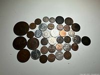 37 assorted coins laid out on white surface showing different sizes, materials and designs.