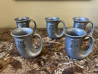 Five metal Michelob cups on a marble surface, showing front and side views highlighting the shape and logo.