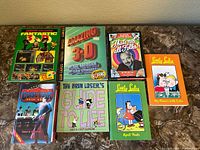 The complete group of 7 children's books arranged on a surface: two 3D books with glasses and five other comic/cartoon books, all colorful and suitable for children or collectors.