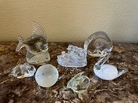 All seven glass paperweights arranged on a marble surface, showing clear glass animal shapes and a frosted sphere with stars.