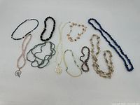 Group of nine costume jewelry necklaces arranged on white surface, showing variety of bead colors and styles.