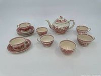 Photo showing the full group of red transferware items including teapot, six teacups, and seven saucers arranged on a white surface.