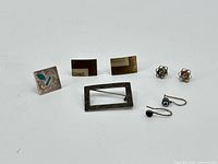 Lot of seven assorted jewelry pieces on white background including brooch, cufflinks, stud earrings, dangle earrings, and ring.