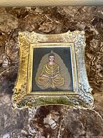 Full view of the framed Buddha leaf painting on a marble surface, showing ornate gold frame and painted leaf with Buddha figure.