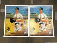 Two printed posters showing the same Oakland Athletics player with baseball batter action sequences in the background, laid side by side on a carpet.