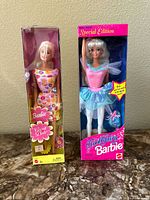 Two Barbie dolls in original boxes shown side by side on a marble surface.