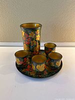 Full set displayed on white surface including pitcher, four cups, and tray showing floral design with yellow interiors.