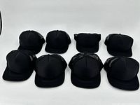 Set of 8 black trucker hats arranged in two rows showing front and side profile.