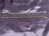 Two vintage sterling silver bracelets displayed side by side on a purple fabric background. The top bracelet is a macaroni link style with thick twisted links, the bottom is a charm bracelet chain without charms.