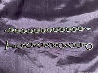 Two vintage sterling silver bracelets displayed on purple fabric, showing circle link styles and toggle clasp.