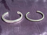 Photo showing both sterling silver bracelets: one solid squared cuff and one twisted cable cuff with gold ends.