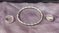 Photo showing two sterling silver domed rings with different band widths and the twisted cable hinged bangle bracelet displayed on purple cloth.
