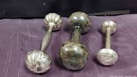 Photo showing front angle view of three tarnished sterling silver baby rattles on dark purple cloth, highlighting the differing end designs.