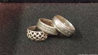 Photo of three sterling silver rings arranged on black surface, showing different band designs and sizes.