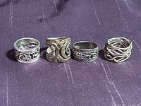 Four vintage sterling silver rings displayed in a row on dark fabric. Each ring shows unique intricate designs and open patterns.