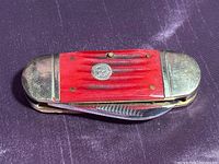 Closed red Frost Cutlery pocket knife with metal bolsters and handle medallion visible.