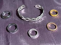 Six rings and one cuff bracelet placed on a dark purple surface, showing all items in the lot.
